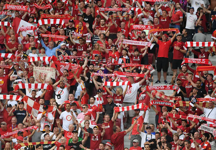 Liverpool football fans hold up their scarves.