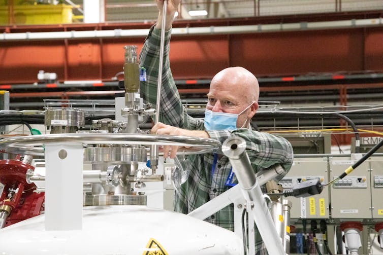 A man inserts a rod into a container of liquid hydrogen in a lab