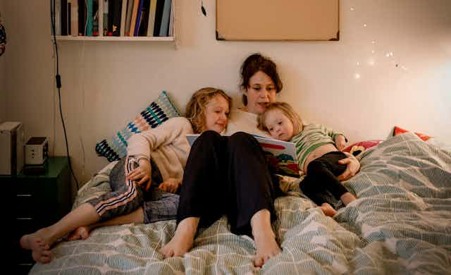 A woman reads to her children in bed