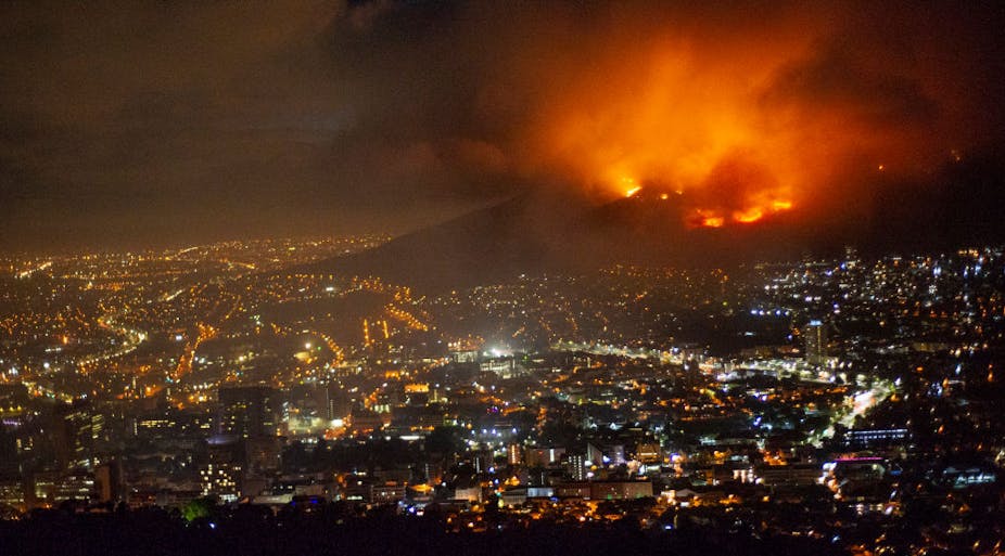 A raging fire at night time burning on the mountain. Below is the brightly lit city.