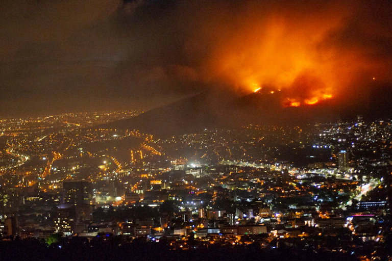 A raging fire at night time burning on the mountain. Below is the brightly lit city.