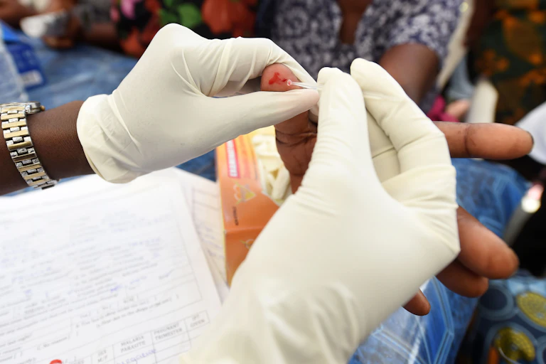 Hands in surgical gloves take blood from finger of another person