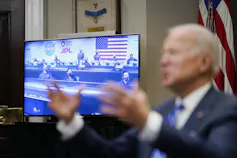 Biden gestures with footage of the Mars Perseverance team on a screen behind him.
