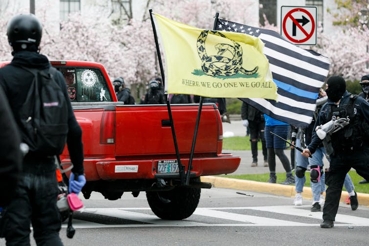 A truck bearing a QAnon flag is chased by anti-fascist counterprotesters down a street in front of the Oregon state capitol building.