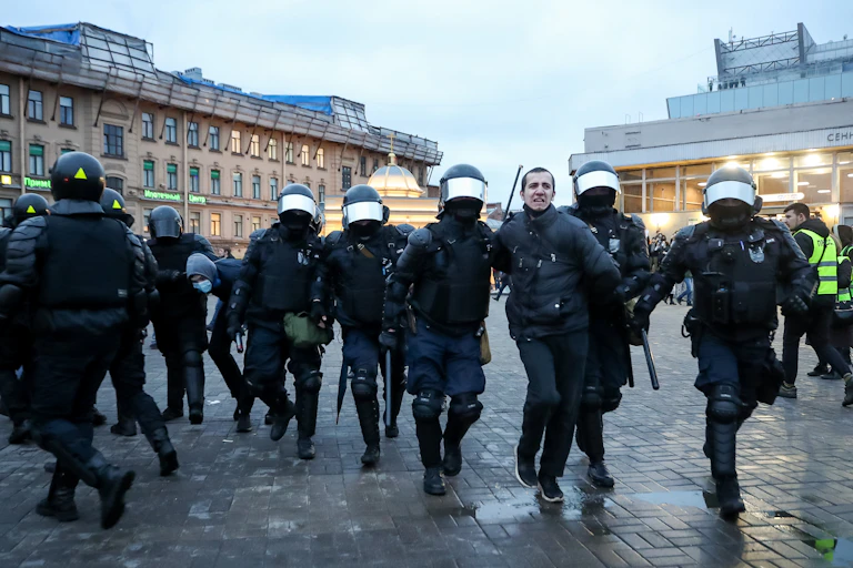 Police in riot gear walk a man in handcuffs through a public square