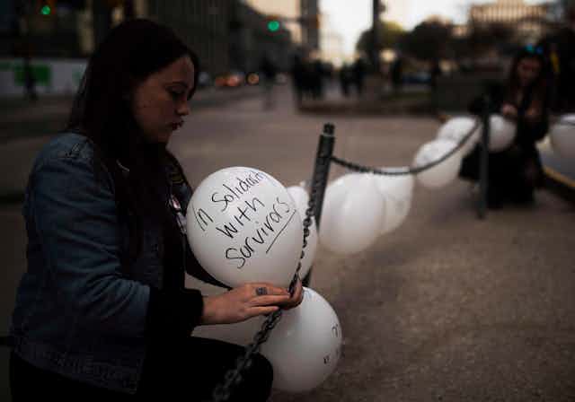 Woman ties balloon that reads 'Solidarity with Survivors'