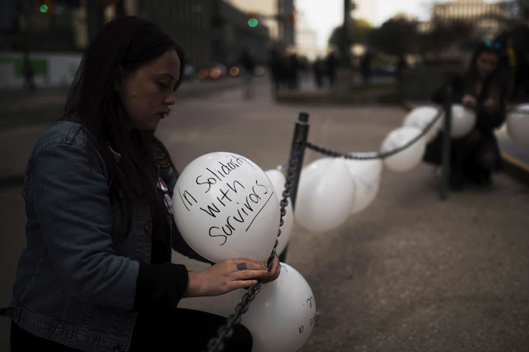 Woman ties balloon that reads 'Solidarity with Survivors'