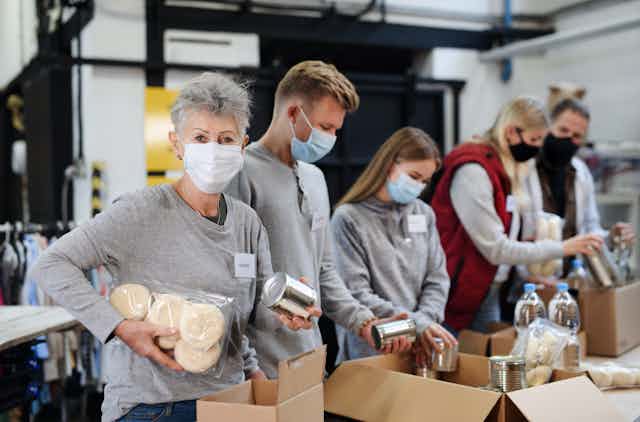 Masked volunteers sort charity donations in a food bank