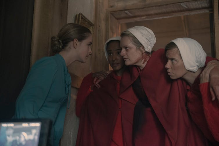 Serena in blue; three handmaids in red.