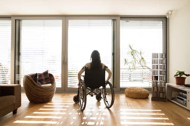 A woman sits in a wheelchair looking out the window.