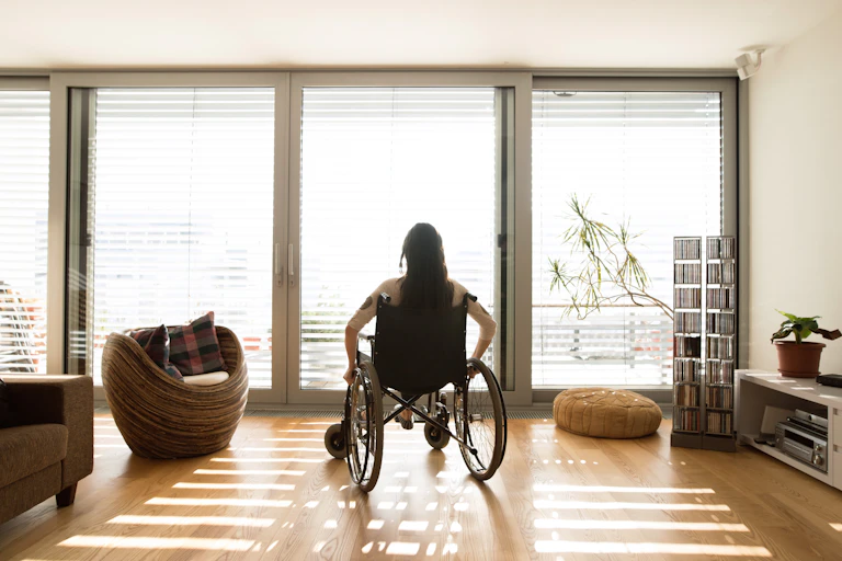 A woman sits in a wheelchair looking out the window.