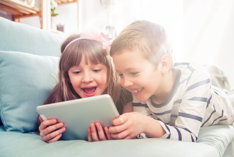 Two young kids (boy and girl) watching something on an iPad.