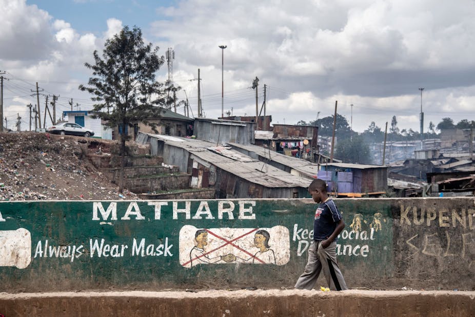 A kid walks by a banner recommending to wear a mask and keep social distance in the streets of Mathare informal settlement