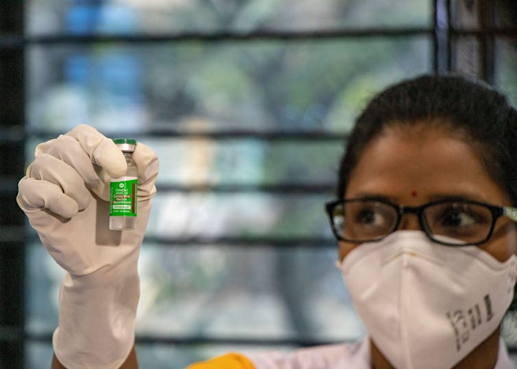 A healthworker wearing a mask holds up a vial of vaccine.