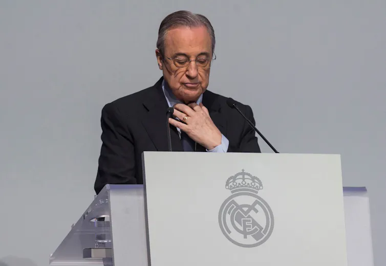 Man in suit standing at lectern looking down.