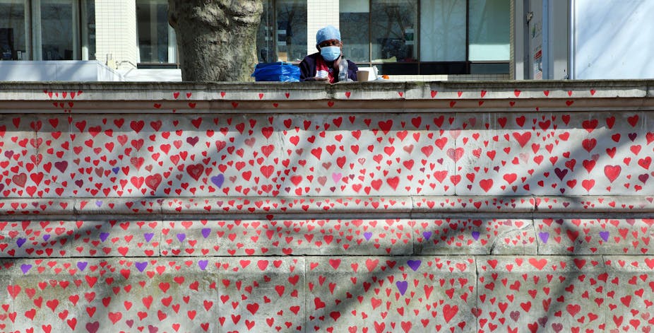 A hospital worker in PPE looks out over Hearts of the National Covid Memorial drawn by the Bereaved Friends and Family of Covid-19 on the embankment of the River Thames opposite the Houses of Parliament.