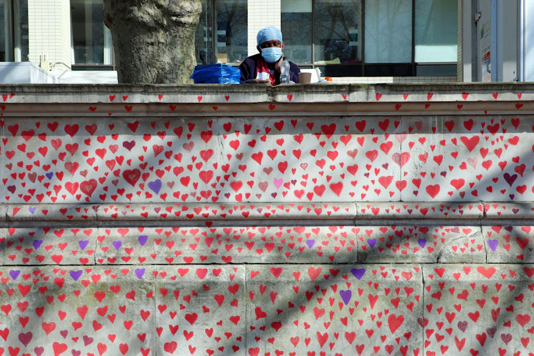A hospital worker in PPE looks out over Hearts of the National Covid Memorial drawn by the Bereaved Friends and Family of Covid-19 on the embankment of the River Thames opposite the Houses of Parliament.