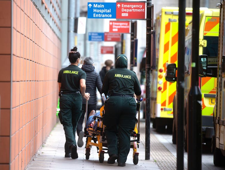 Two ambulance workers wheel a patient into hospital.