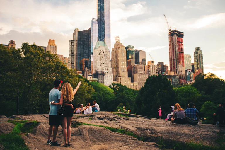 People in Central Park point towards the skyscrapers beyond the trees