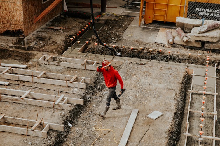 A man in a red top and hard hat walks across a construction site