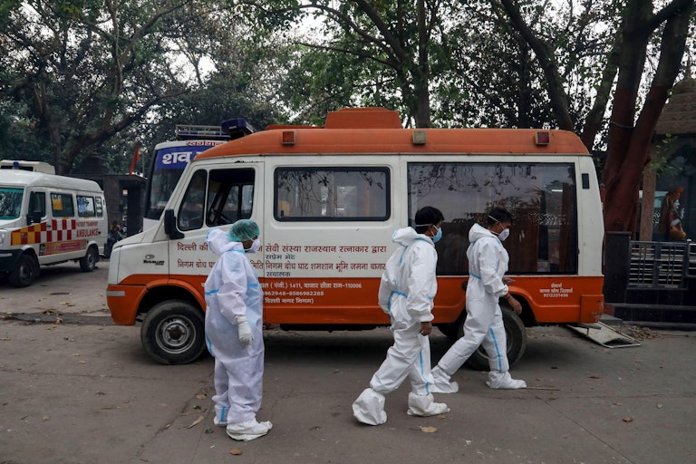 Relatives of COVID-19 victims walk past a van at Nigambodh Ghat crematorium in New Delhi