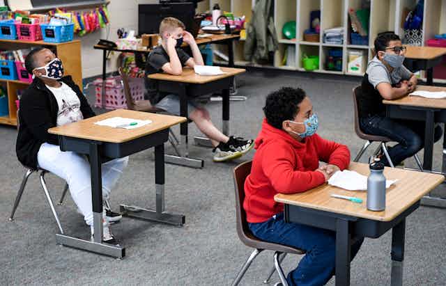 Children wearing masks sit in a classroom.