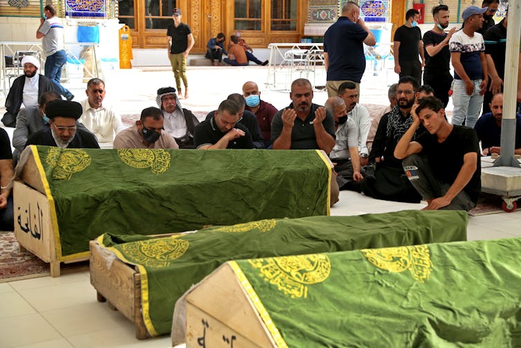 Mourners pray near the coffins of coronavirus patients who were killed in the hospital fire.