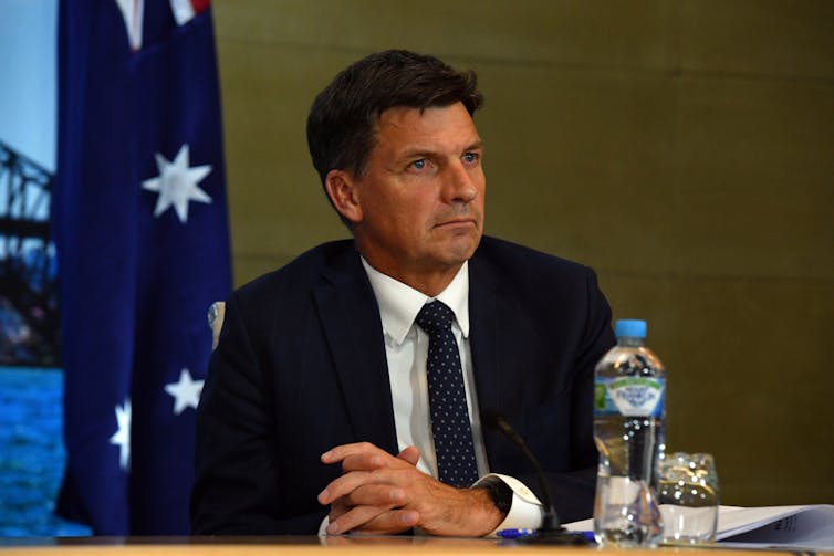 Angus Taylor sitting in front of an Australian flag, with a water bottle