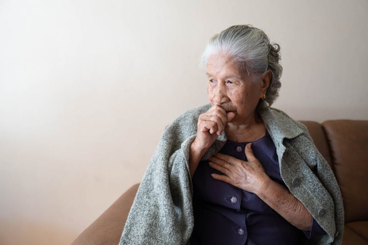 Elderly woman coughing with blanket over her
