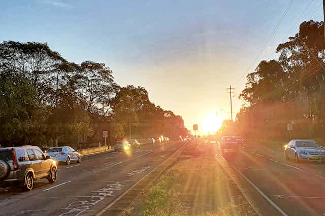 Cars driving at sunset along a divided multi-lane suburban road