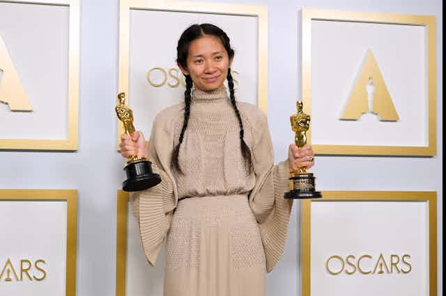 Chloe Zhao posing with her Oscar awards on a red carpet