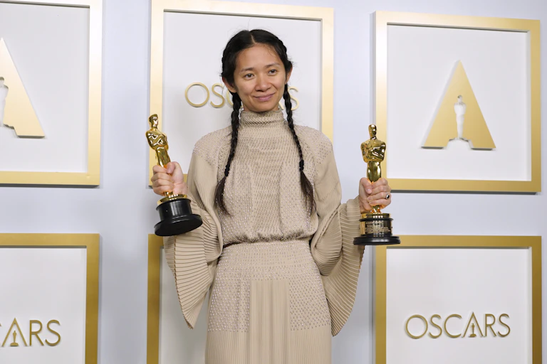 Chloe Zhao posing with her Oscar awards on a red carpet