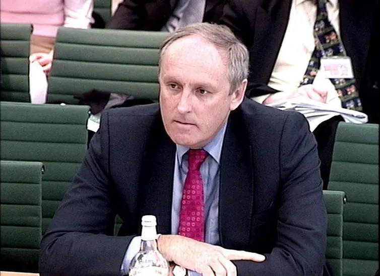 Paul Dacre sat in front of green chairs of parliamentary committee room.