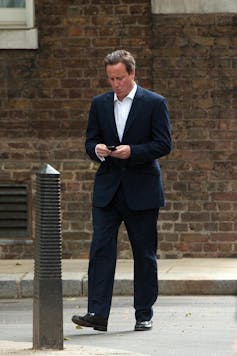 David Cameron walking down the street looking at his phone, appearing to text.