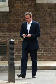 David Cameron walking down the street looking at his phone, appearing to text.