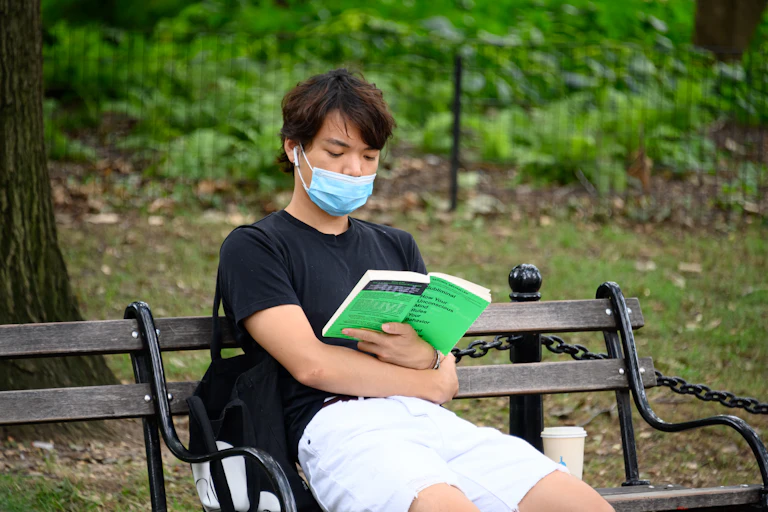 Person wearing face mask reads on park bench