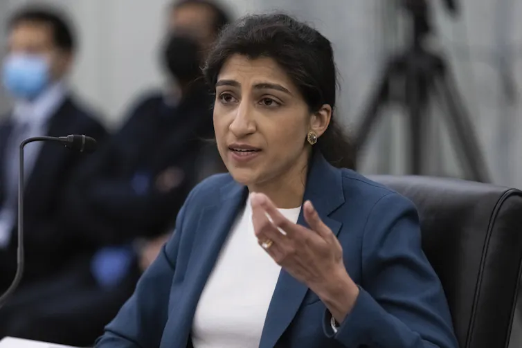 A seated woman gestures with her left hand as she speaks into a microphone