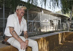 Joe Exotic sits in front of an exotic animal enclosure.
