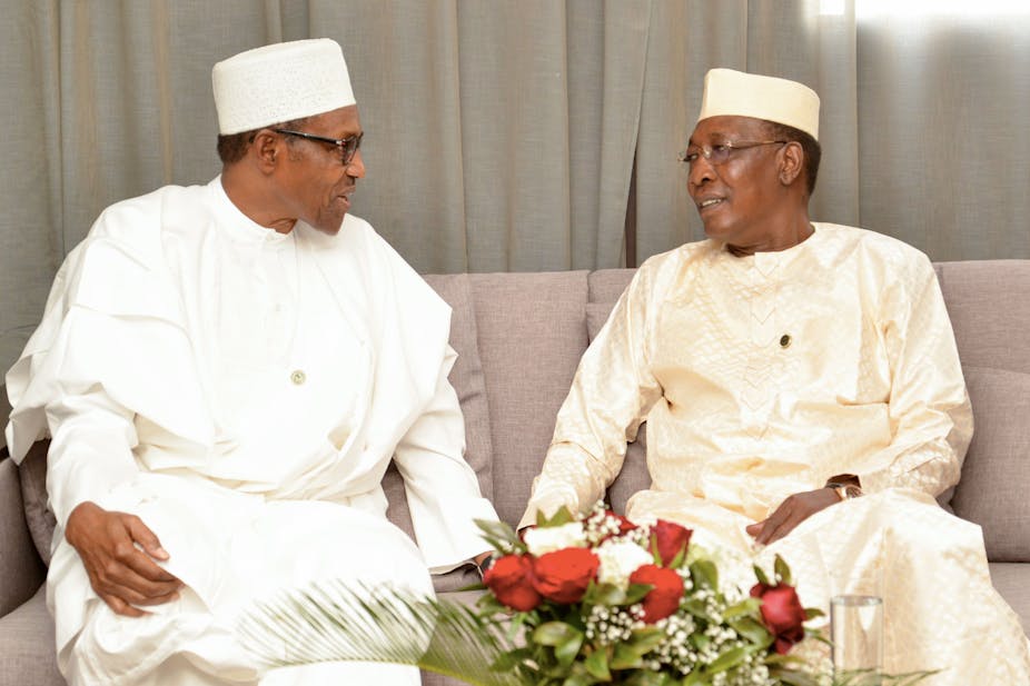 Two men wearing white traditional attires with caps, having a discussion. 