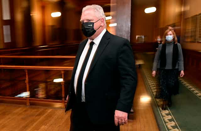 Doug Ford and Christine Elliott, in masks, walk towards the media at Queen's Park.
