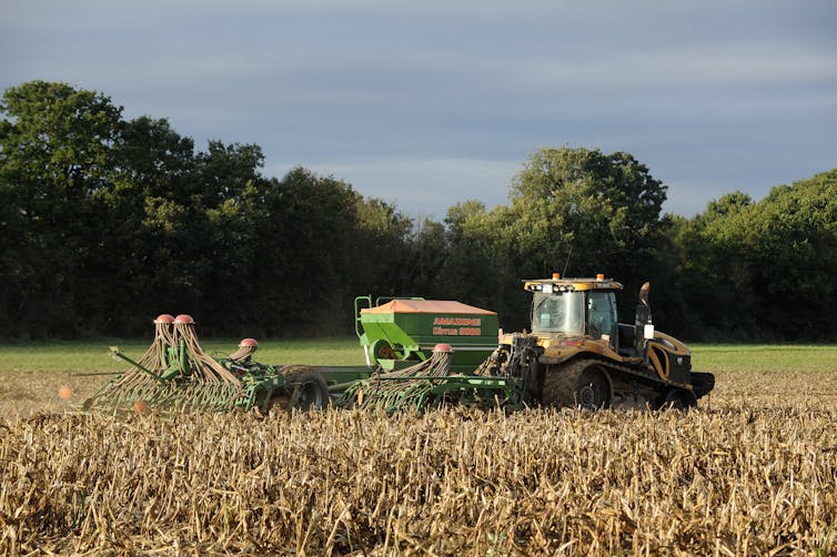 A tractor with a mechanised seed drill in tow prepares a field for sowing.