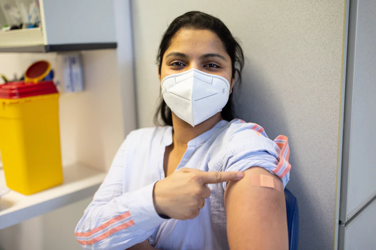 masked woman points to her vaccine bandaid