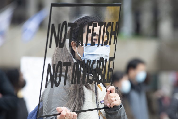 Woman stands holding protest sign
