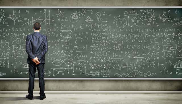 Businessman looking at complex equations on blackboard.