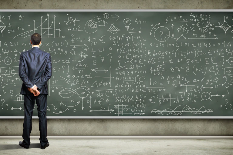 Businessman looking at complex equations on blackboard.