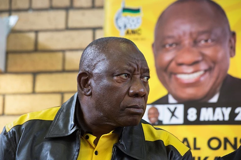 A man wearing a black and gold leather jacket and matching T.shiort gioves a stern look.