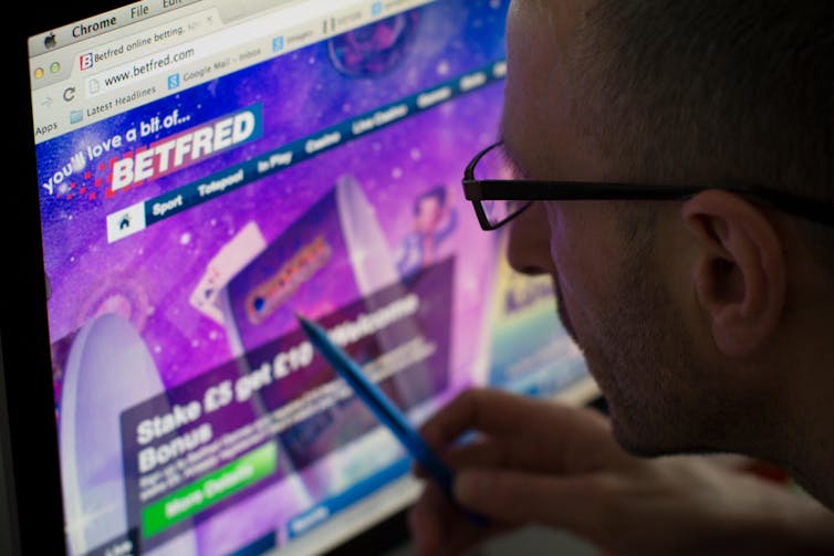Man wearing glasses points pen at Betfred website on computer screen