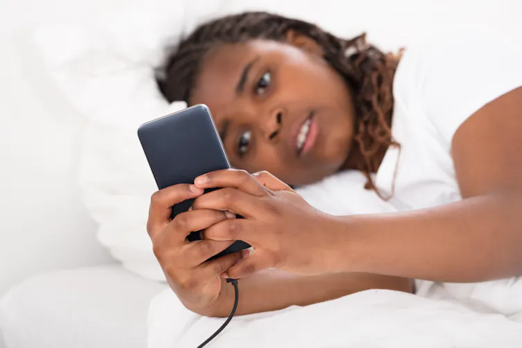 A girl lies in bed looking at her phone