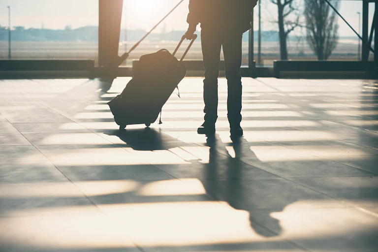 A passenger stands with a suitcase in an airport departure lounge.