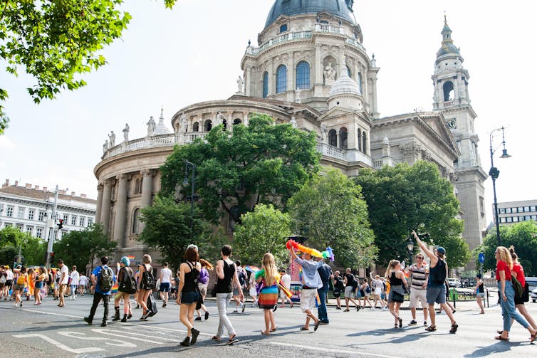Men and women walk through city street, some with rainbow flags and clothing.